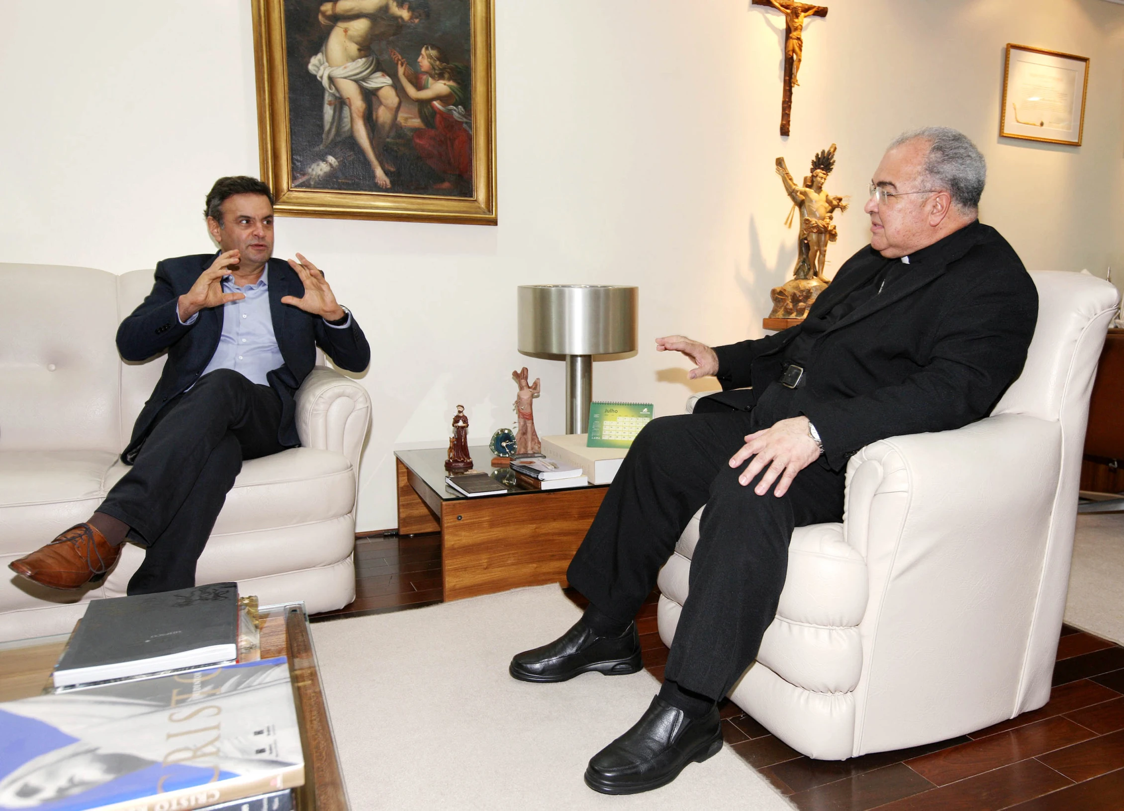 two men in suits talking together in a room with paintings on the wall