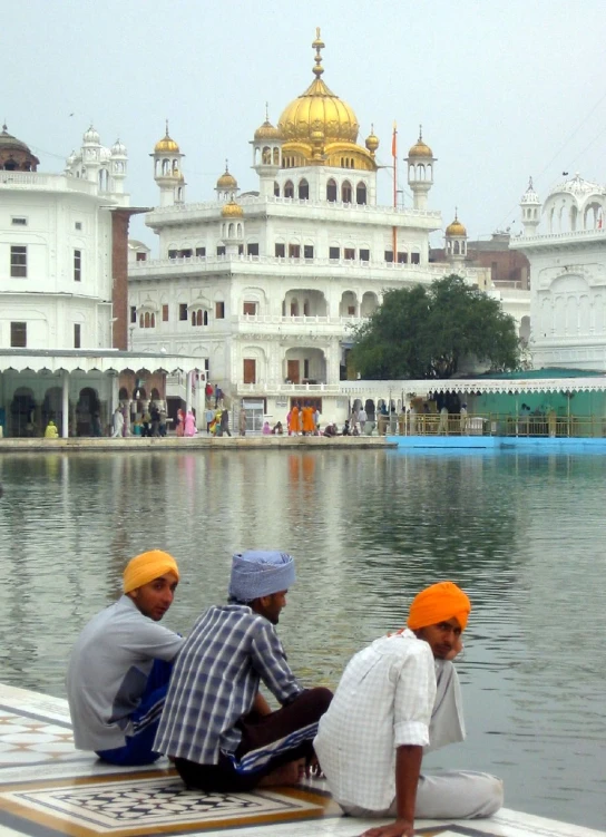 men sitting on the edge of a lake with an elaborate building in the background