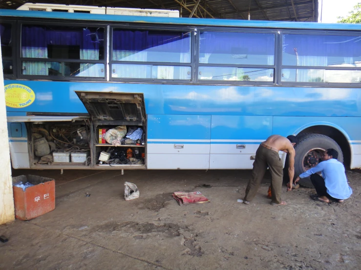 two men fixing the flat tire of a blue bus