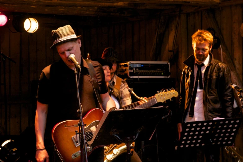 four men wearing hats singing on stage with instruments