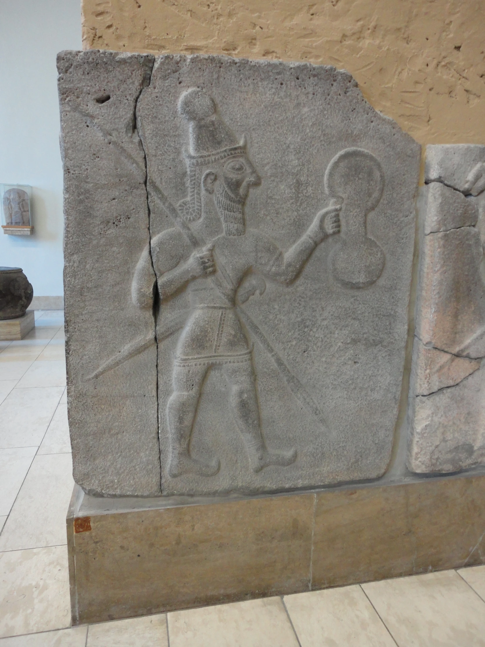 ancient stone carving displayed on cement block with vase in background