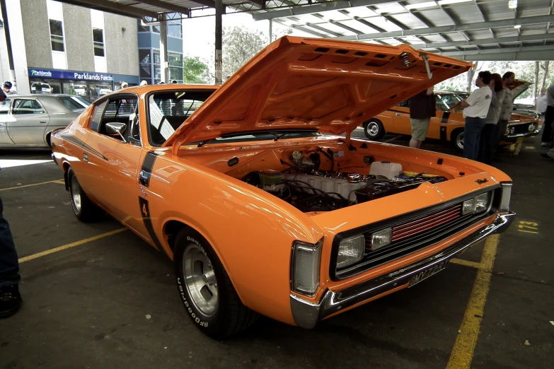 an orange muscle car with its hood up at a gathering