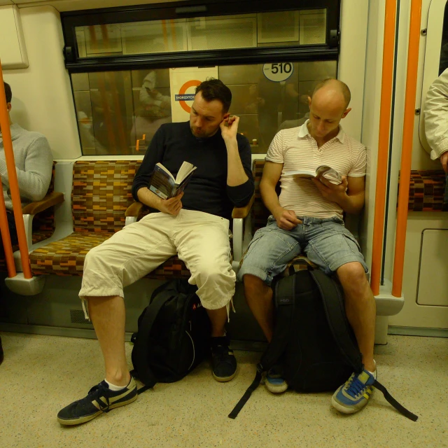 a man reading a book sitting on a bus next to another person