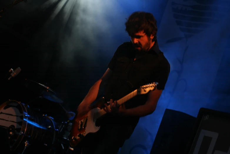 a man standing in front of a blue light holding an electric guitar