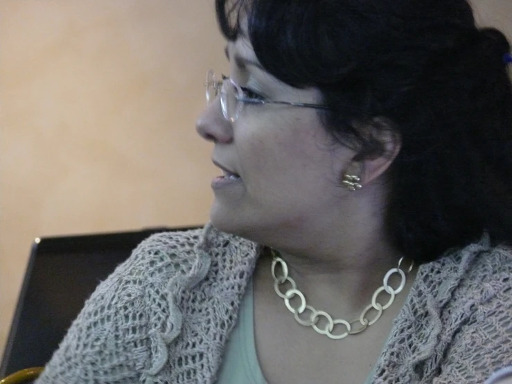 a woman with glasses wearing a necklace is looking to the side