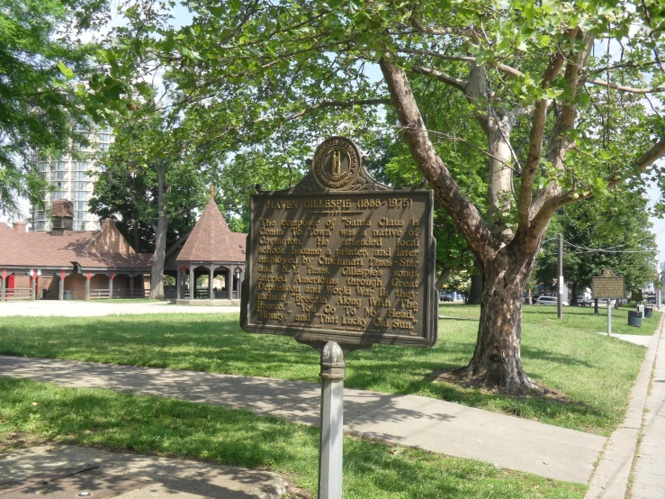 a brown sign in the grass near a tree