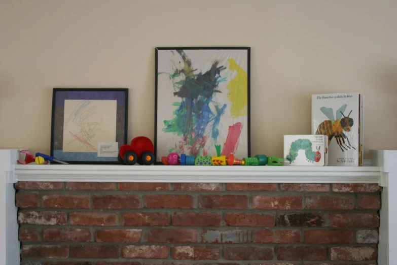 a brick fireplace surrounds a picture and various framed works