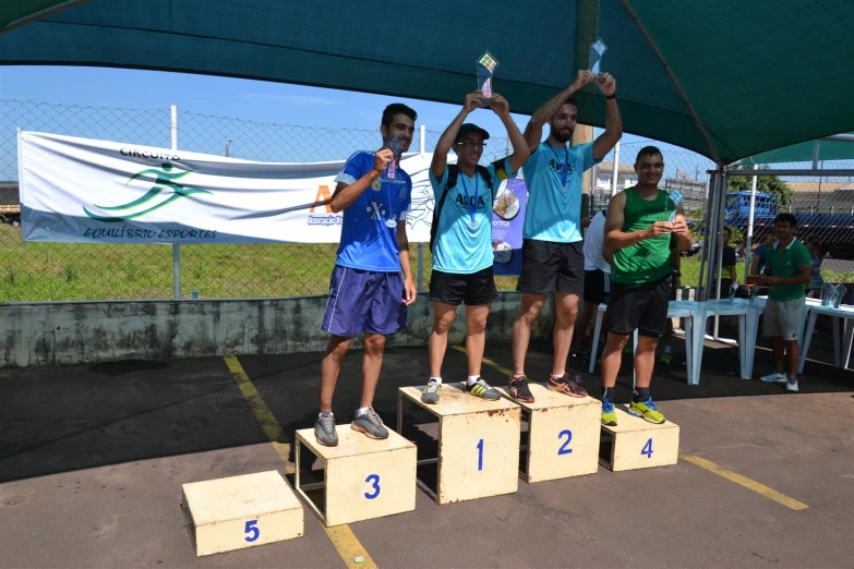 four young men holding their medals on wooden blocks