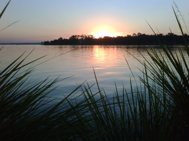 the sun is setting over a lake surrounded by trees