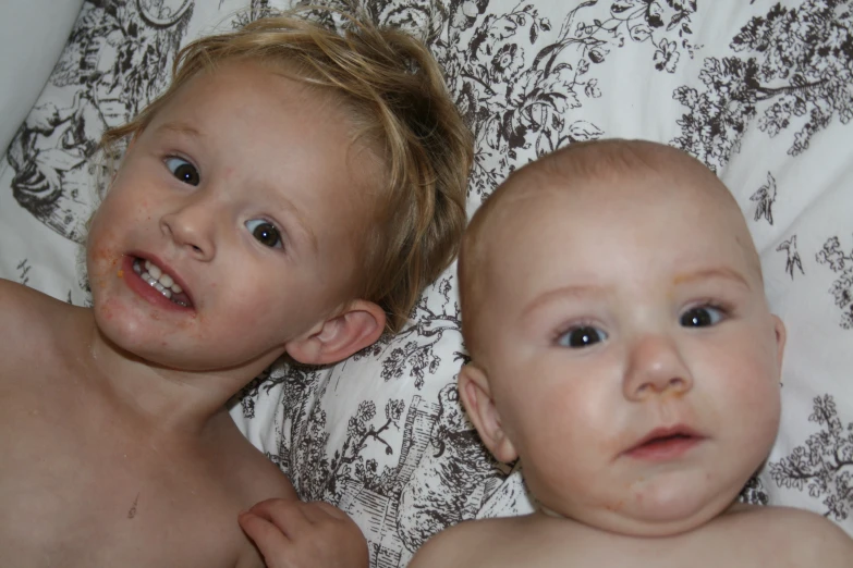 two children are lying on the bed with their heads tilted