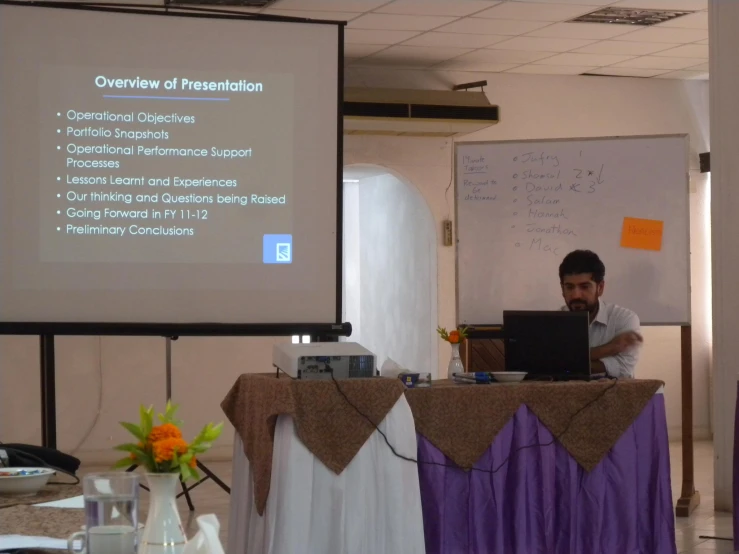 a man is in front of a screen while using a laptop