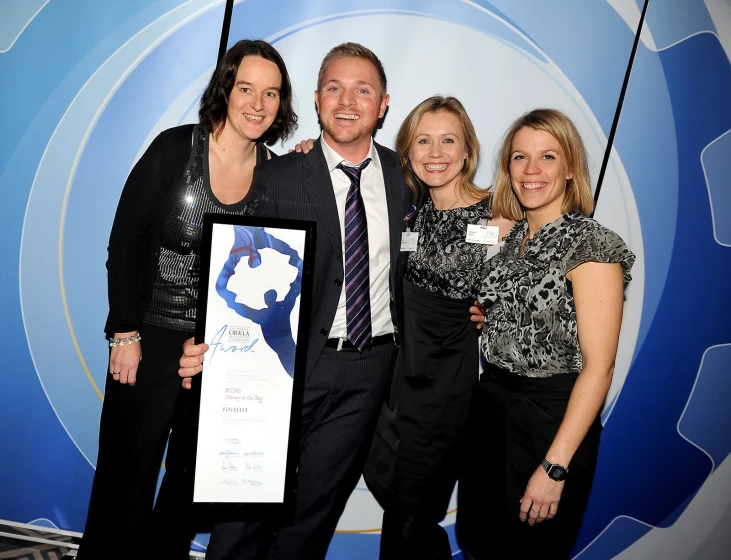 three people smile with one of them holding an award