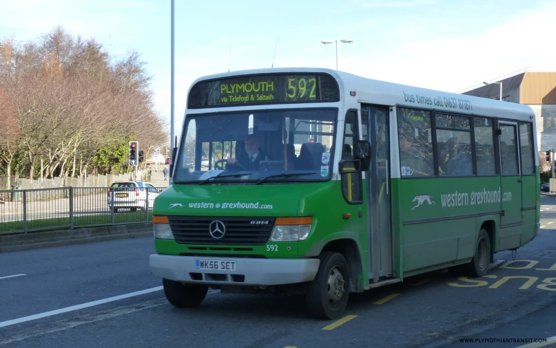 a green bus is on the road by a fence