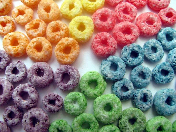 a rainbow of colored donuts are placed in rows