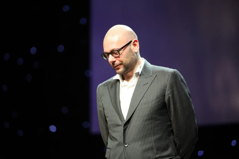 a bald man wearing glasses on stage