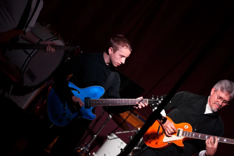 the two men are playing guitar together in the dark