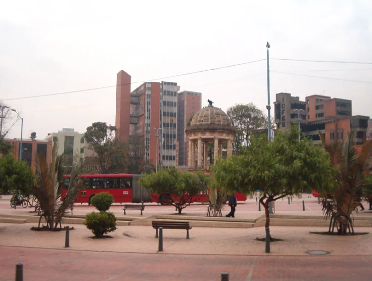a view of a park with trees, benches and a red bus in the distance