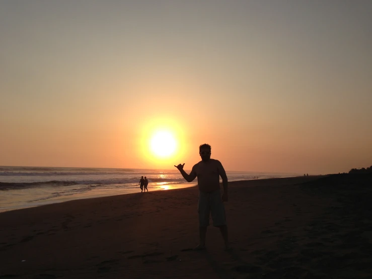 the silhouette of a man standing on a beach flying a kite