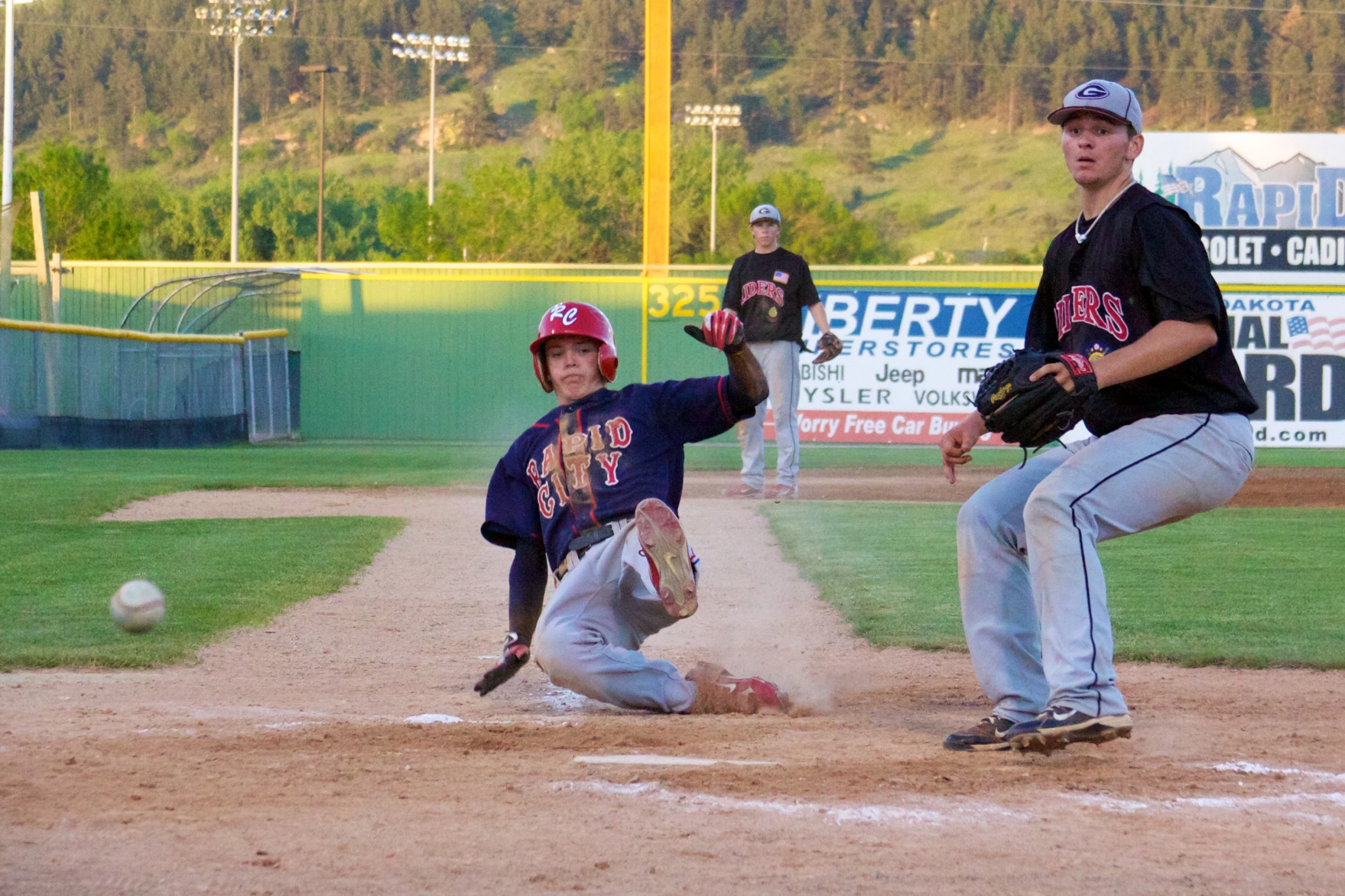 a boy on the ground trying to slide into base as another runs away