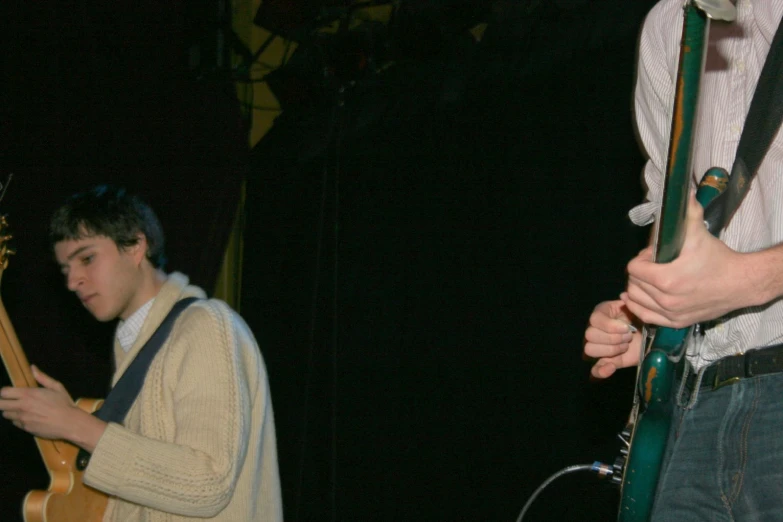 a boy in a white shirt plays guitar while a man in a yellow sweater looks on