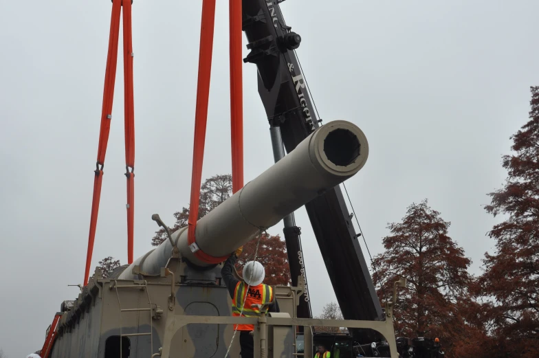 a crane lifting a metal pipe onto the back of a large truck