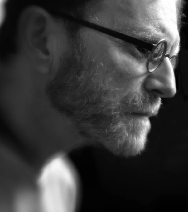 a close up of a person wearing glasses looking over his shoulder