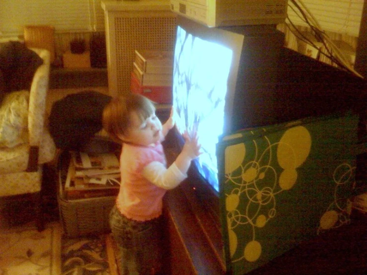 a little girl standing on a chair and holding a television