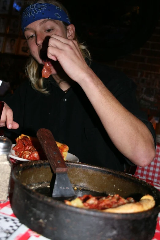 a woman eating food from a pan while standing in front of a basket