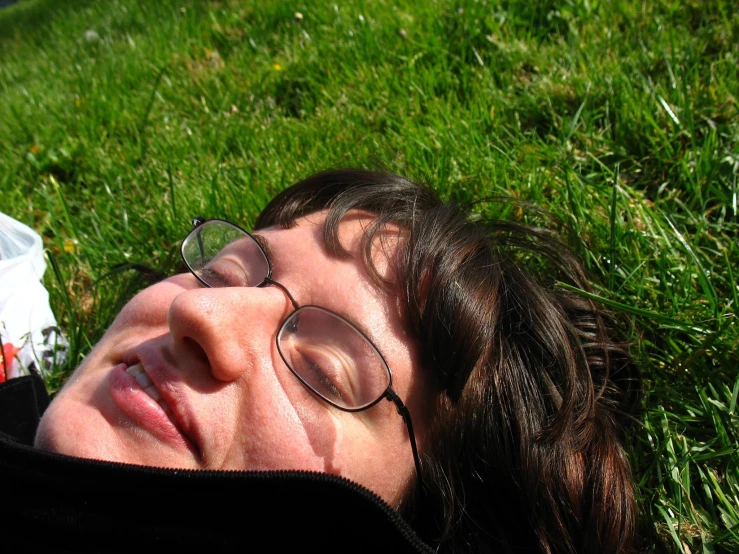 a person wearing glasses laying on the grass