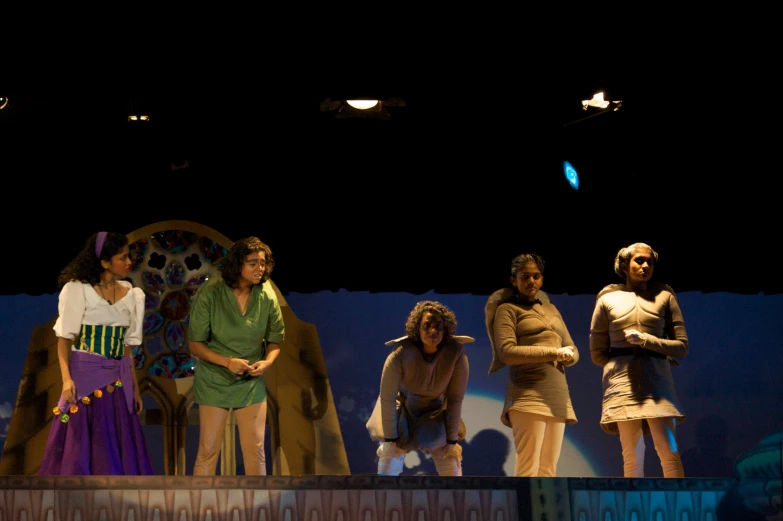 five women dressed in old fashioned clothing and dark lighting on a stage