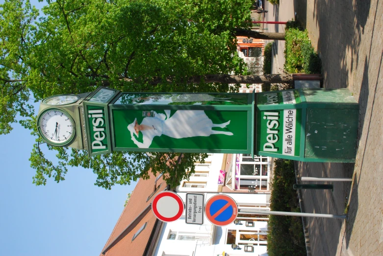 a large green street sign next to a clock