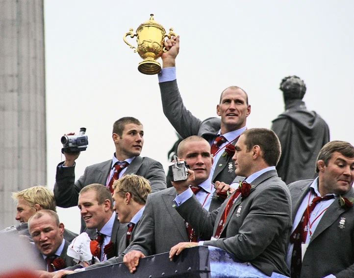 men in suits and ties stand holding up a trophy while being pographed