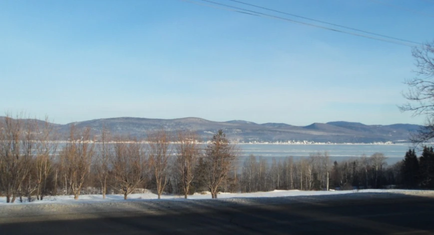 a view of water, snow, and mountains from an empty street