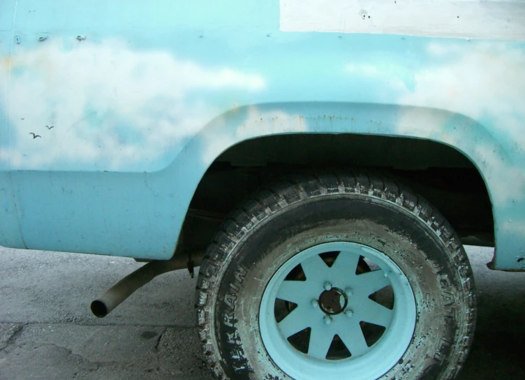 a blue truck with a rusted metal rim sitting on a sidewalk