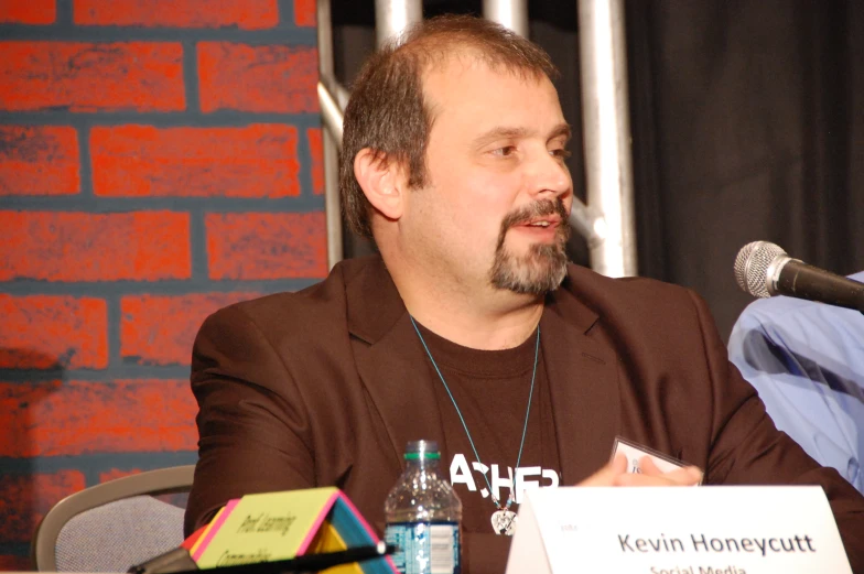 a man in brown jacket speaking on stage