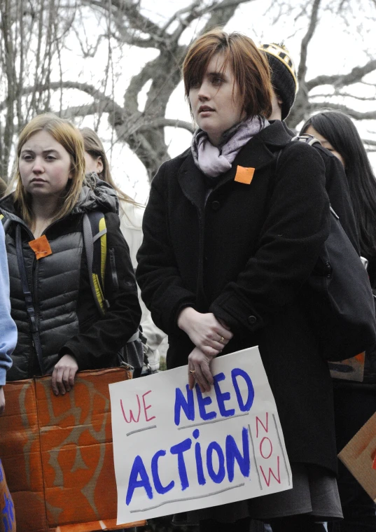 a woman stands holding a sign that reads we need action now