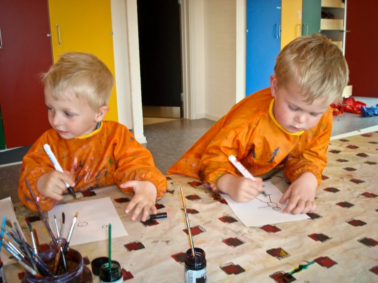 two boys are drawing on paper at a table