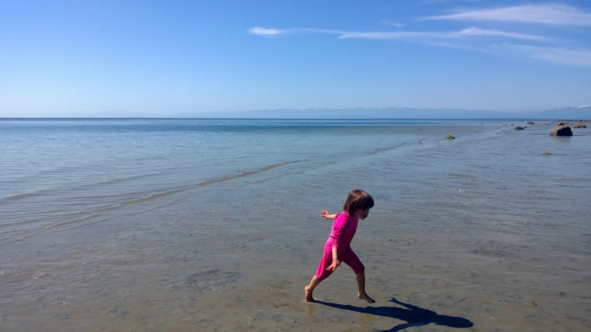 a little girl standing on the shore in front of the ocean