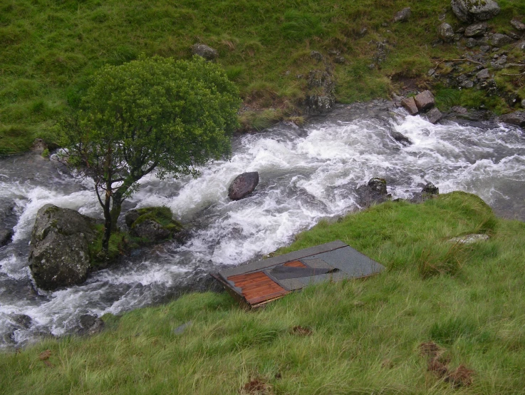 an outdoor toilet in the grass near a river