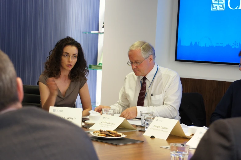 an older man and two women sit at a table discussing