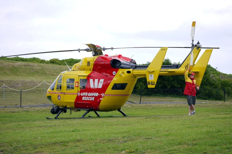 the man stands in front of a red and yellow helicopter