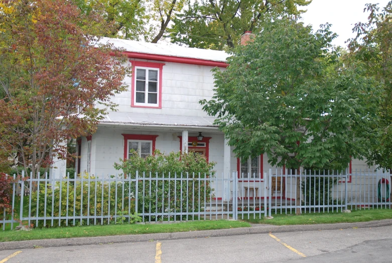 a white house with red trim and windows, has picket fence on the street