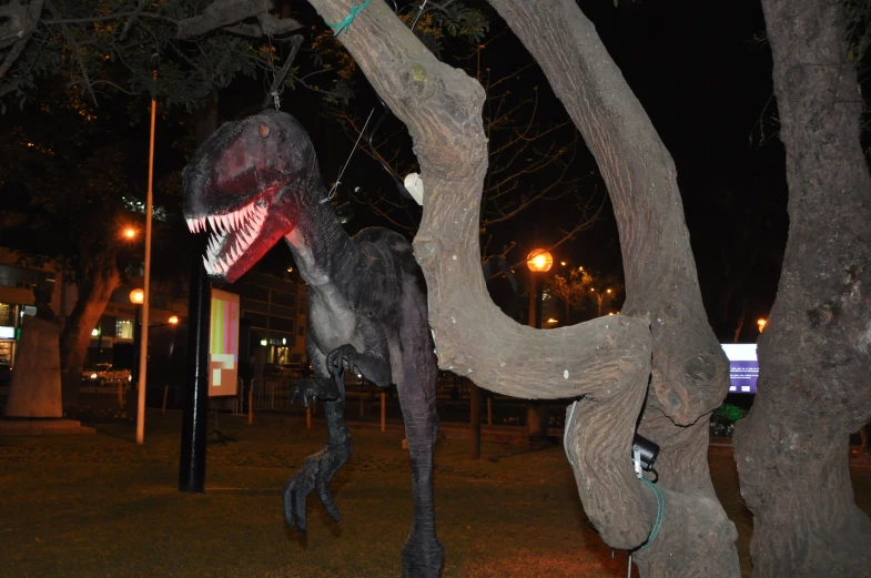 dinosaur statue displayed next to large tree at night