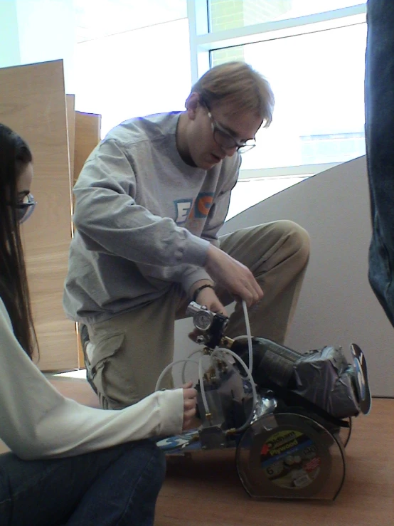 man with glasses working on small machine with woman standing next to him