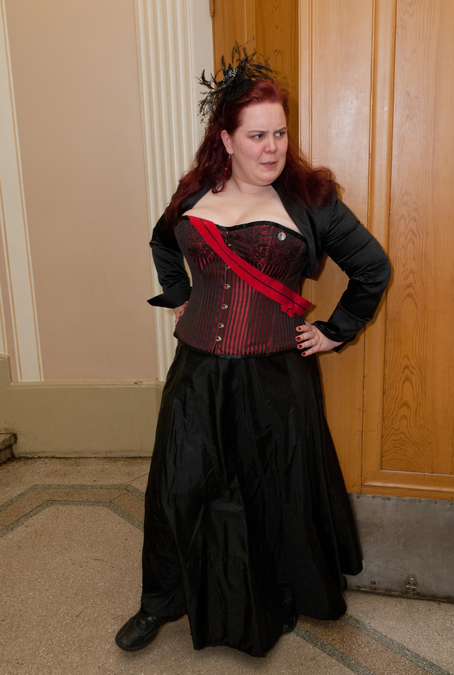 a lady in black and red corset standing by the wall