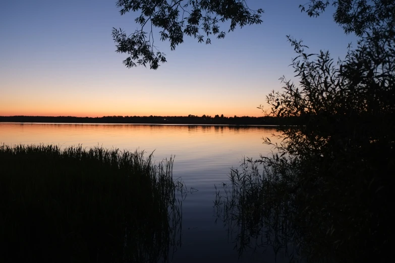 the sun rises over a calm lake that reflects the sky and trees