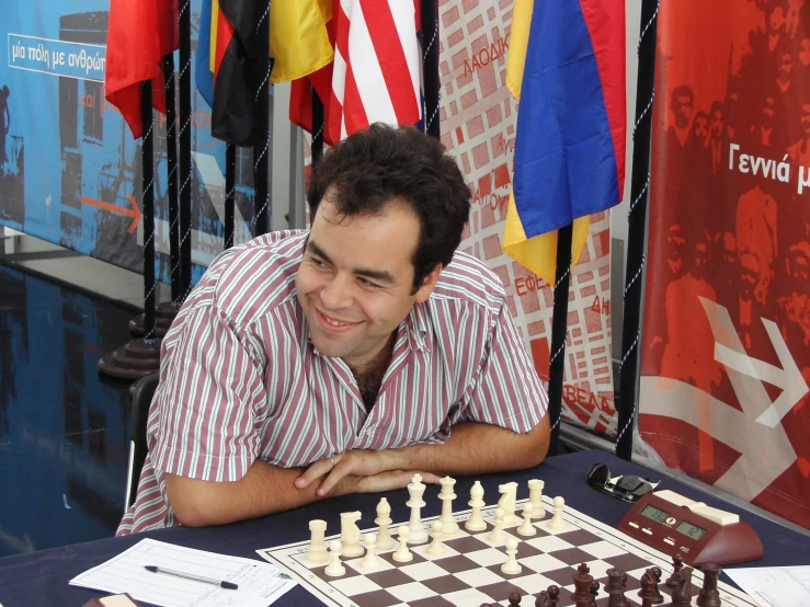 a man smiling while sitting at a chess table