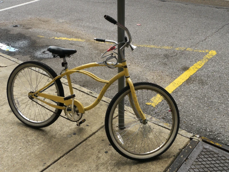 a yellow bike parked next to a pole in the sidewalk