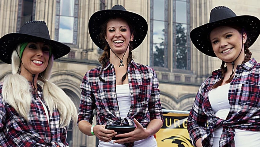 three women with cowboy hats smiling and wearing large black hats