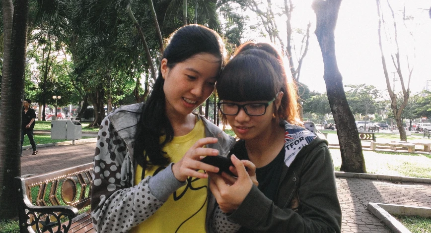 two asian women stand next to each other while looking at their phones